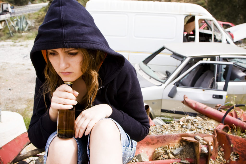 sad young woman drinking in scrapyard